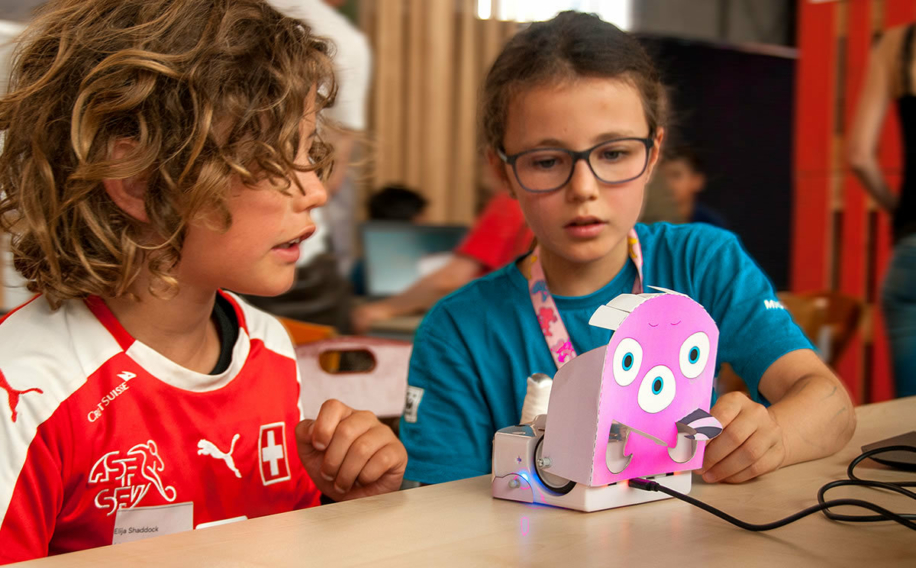 Junge und Mädchen vor einem Thymio-Roboter, der als Alien dekoriert ist
